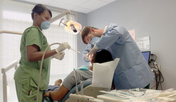 A dentist and assistant clean a young patient's teeth