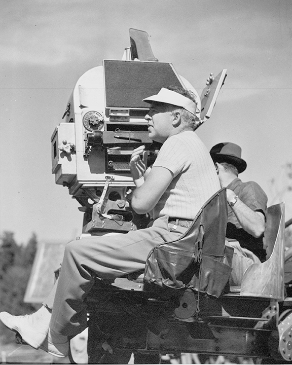 Clarence Brown seated at a camera on a production set