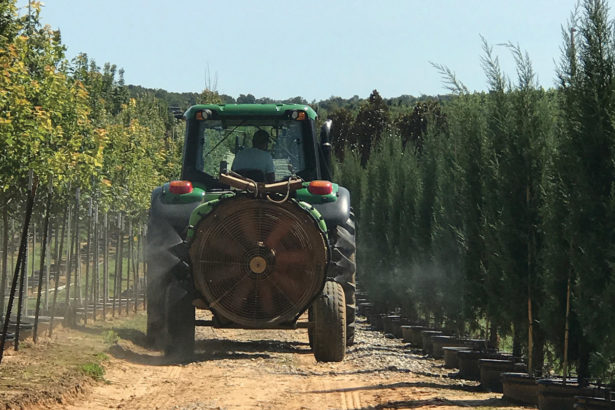 a pesticide sprayer mounted on the back of a tractor drives between rows of crops
