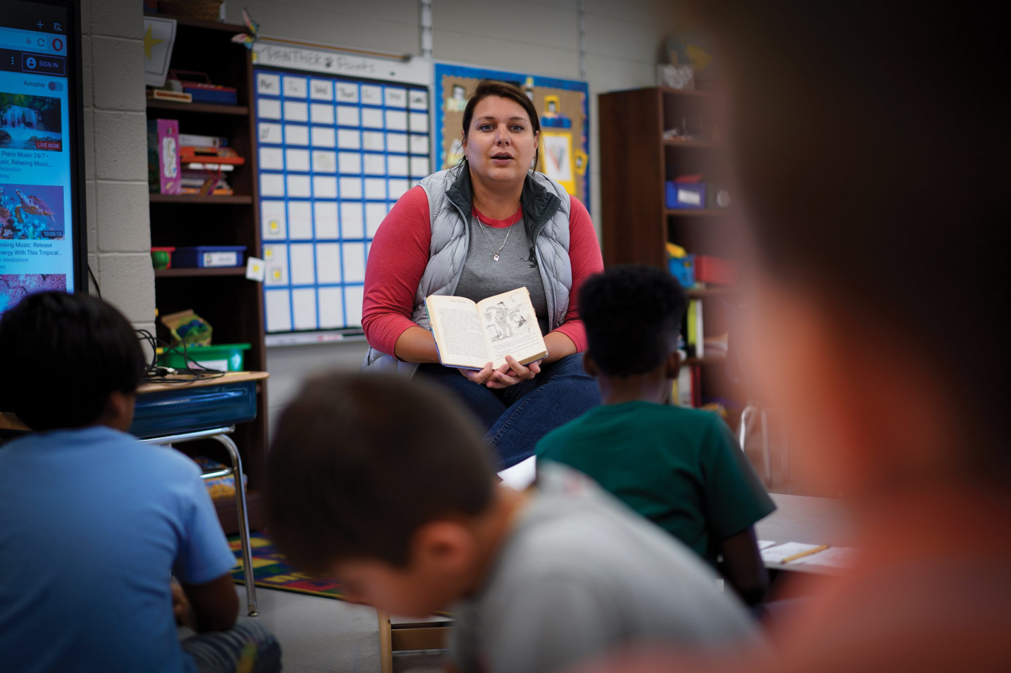 A teacher holds a book open to an illustration as she reads to a classroom