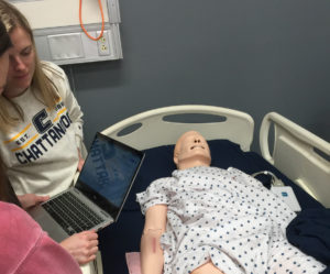 UTC students stand in front of a medical simulation mannequin