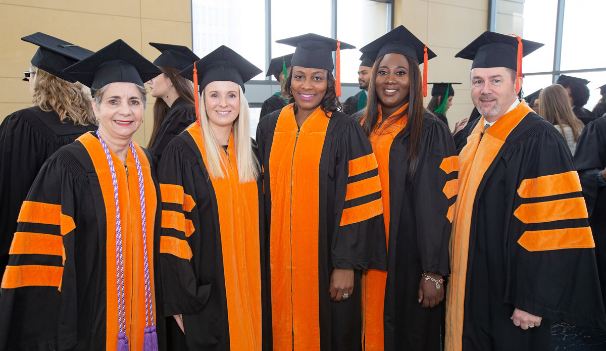 Five doctoral graduates in black graduation gowns and orange stoles