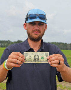 A main in a hat and sunglasses holds up a U S dollar bill
