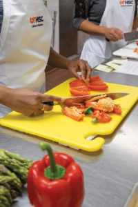 A student dices a red pepper on a cutting board